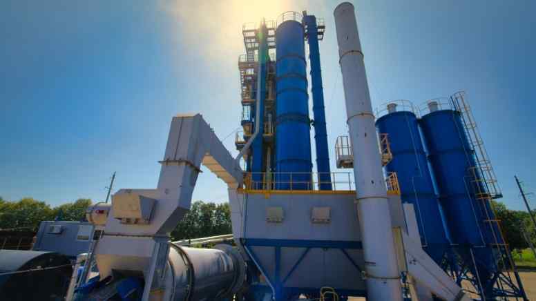 Centrale Denrobage Fix Industrial cement plant with tall blue silos, a conveyor system, and metal staircases under a bright sky.